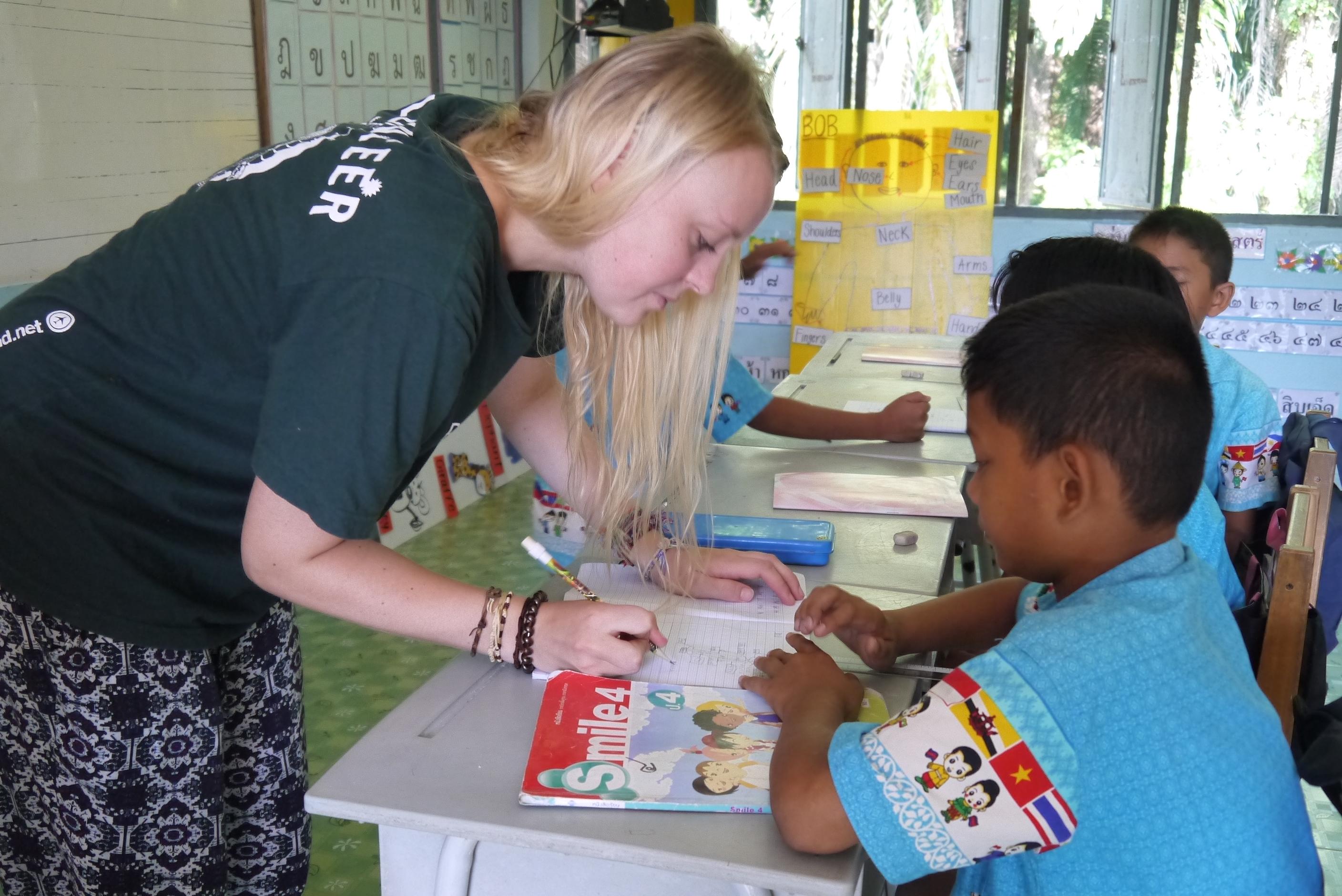 Projects Abroad volunteer teaching in Thailand marks the classwork of a young student. A volunteer corrects the work of her students during her teaching work experience in Thailand.